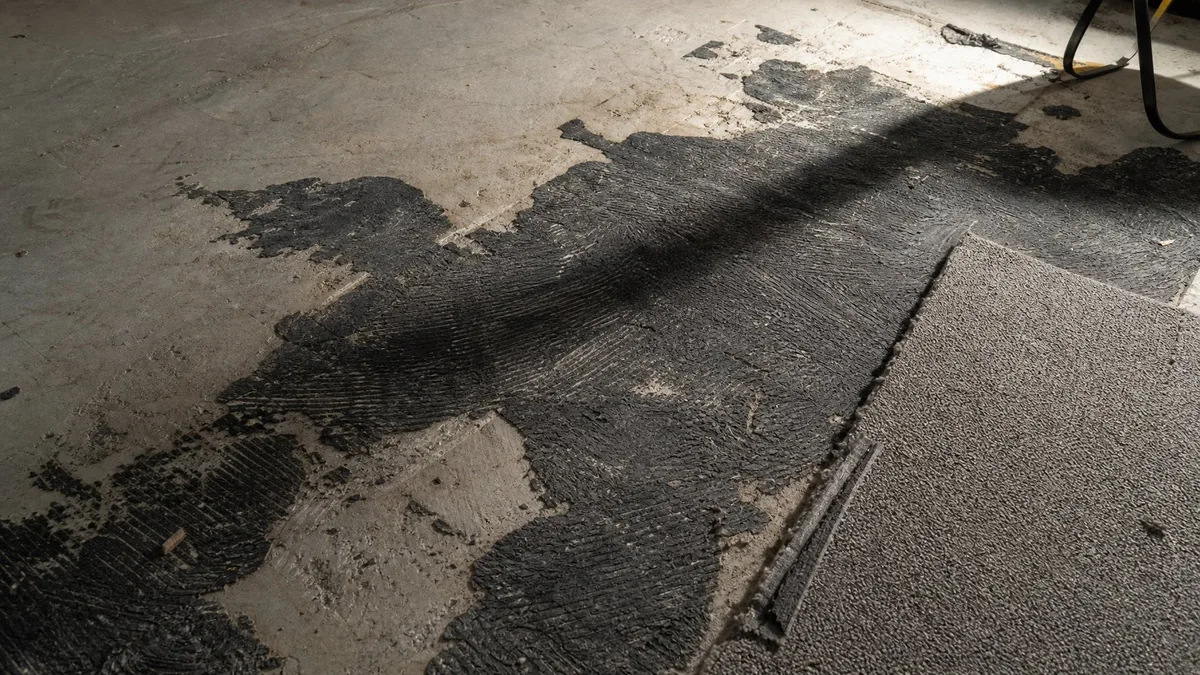 Alter schwarzer Teppichkleber auf Betonboden mit teilweise entferntem Teppichboden in einer Schweizer Altbauwohnung